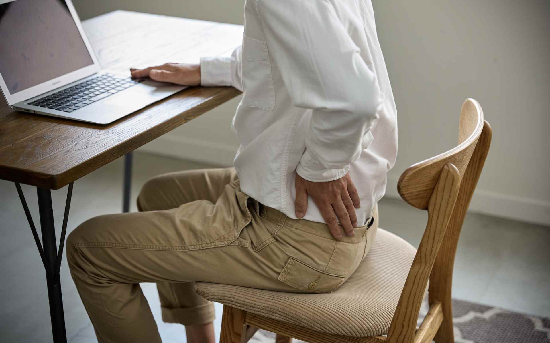 Persona con dolori da rientro al lavoro che si massaggia cervicale e schiena alla scrivania